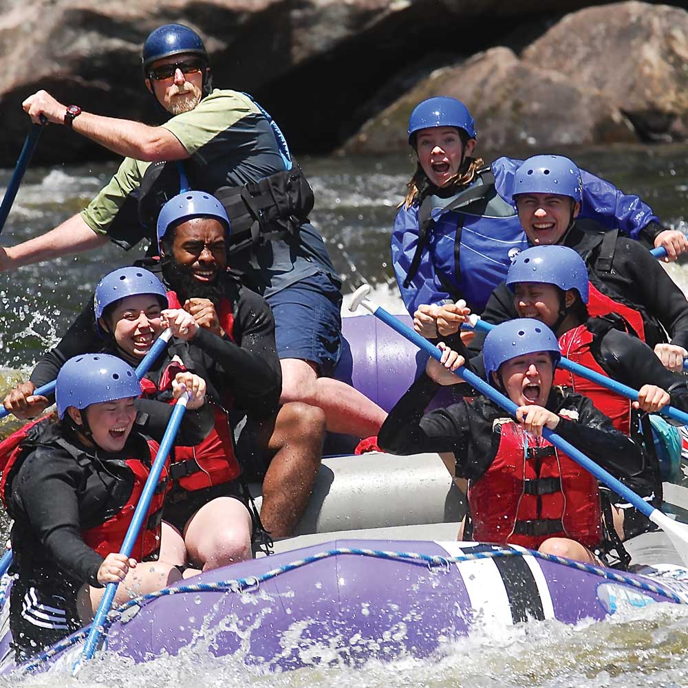 Smiling students in a guided white water raft on a beautiful sunny day