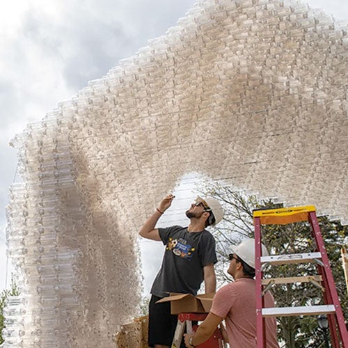 Two students build a house out of recycled bottles